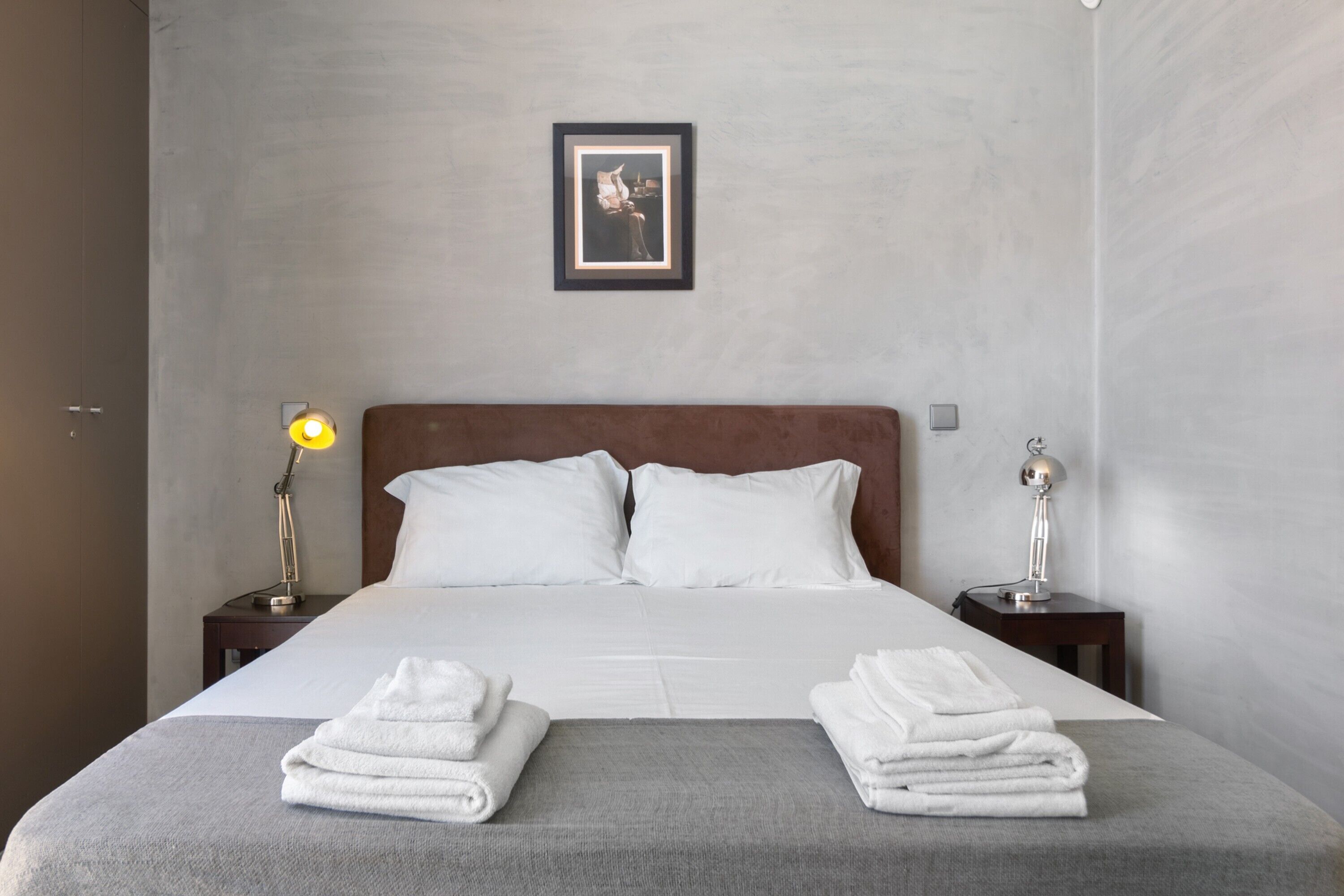 A neatly made bed with white linens, two bedside tables with lamps, and a framed picture on the wall.