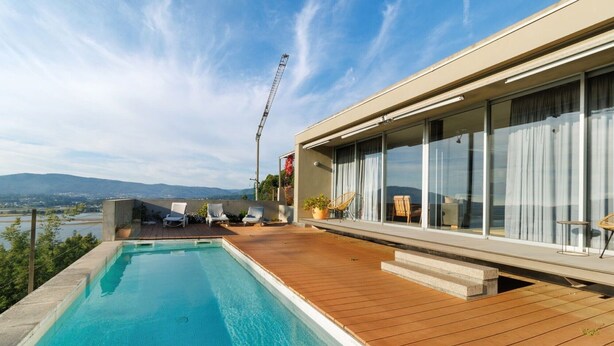 Un espace moderne aménagé au bord de la piscine, avec une terrasse en bois, des chaises longues et une vue sur le paysage.