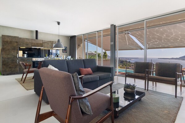 A modern living room with a sofa, armchairs, a coffee table, and a view of the sea.