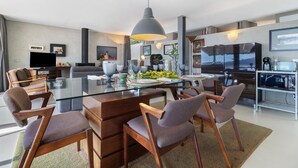 Un salon moderne avec une table à manger en verre, des chaises en bois, un grand luminaire suspendu et une cheminée.