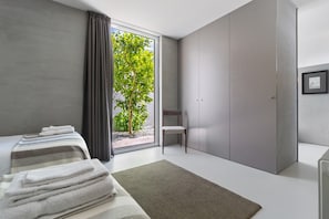 A modern hotel room with a large window, a bed with neatly folded towels, a chair, and a wardrobe.