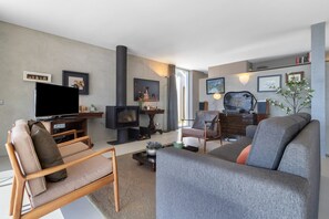 A modern living room with a sofa, armchair, television, fireplace, and artwork on the walls.