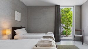 Une chambre d’hôtel avec deux lits, une vue sur la verdure par la fenêtre, une chaise et une lampe.