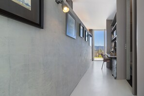 A hallway with a desk, chair, and shelves, leading to a door with a view of the outdoors.