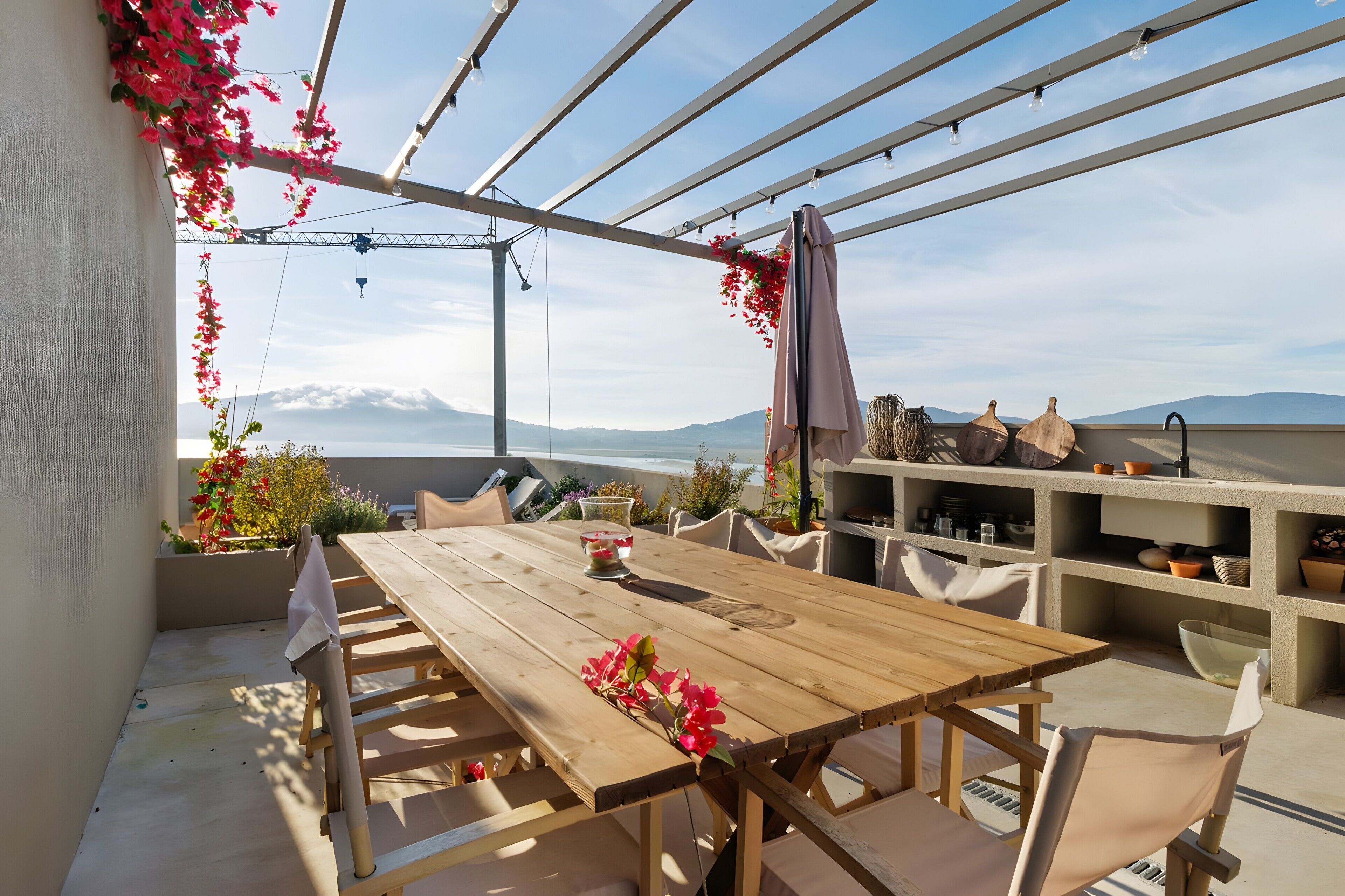 En uteplats med ett träbord och stolar, en pergola med ljusslingor och utsikt över bergen.