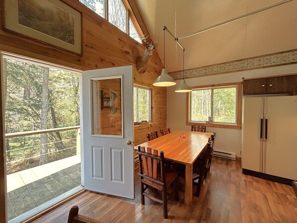 A wooden interior with a large dining table, chairs, a refrigerator, and a door leading to a balcony.