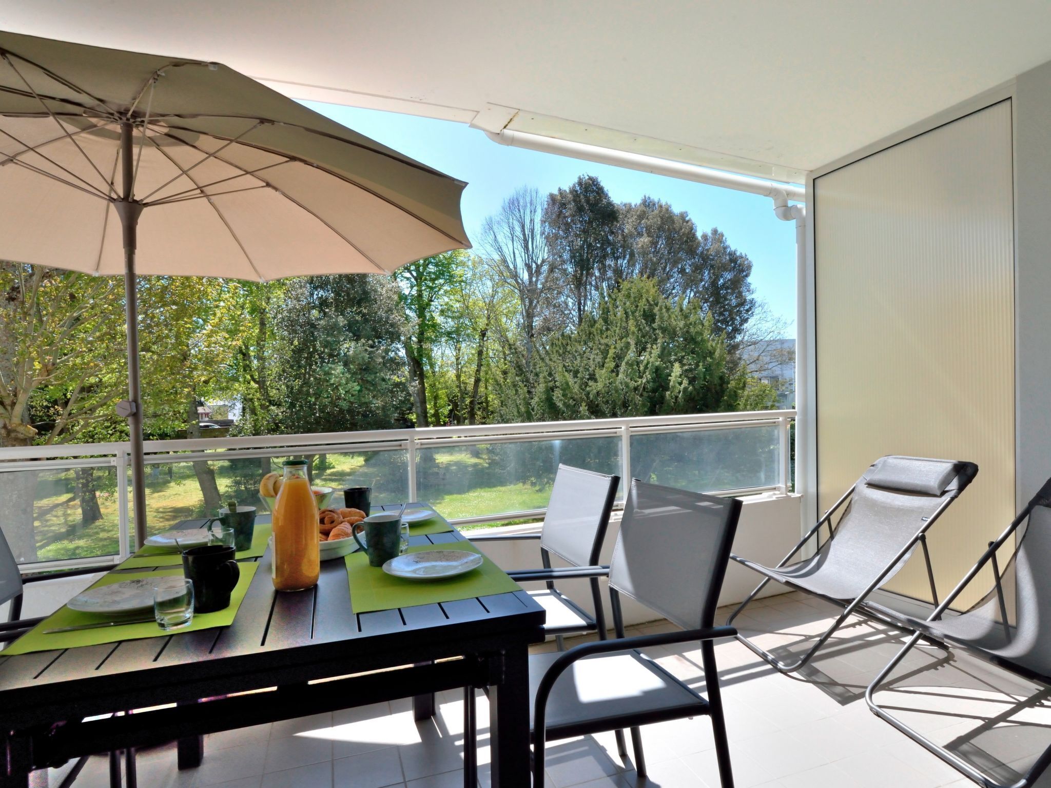 Ein Balkon mit Tisch, gedeckt für ein Frühstück, darunter Croissants und eine Flasche Orangensaft, sowie zwei Liegestühle.