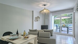 Ein modernes Wohnzimmer mit Essbereich, einer Couch, einem Fernseher und einem Balkon mit Gartenmöbeln.