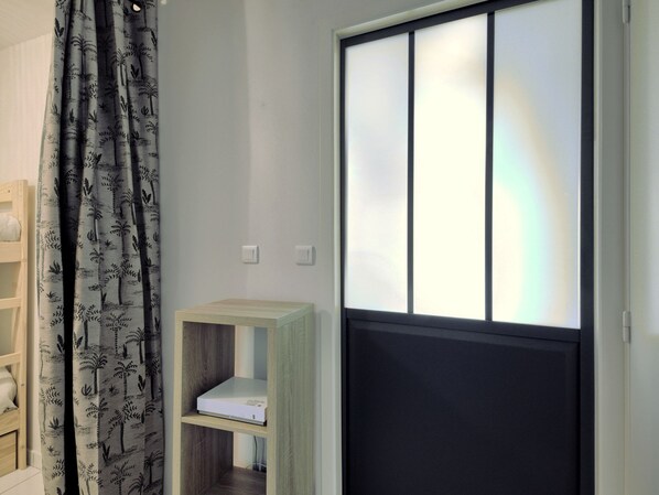Una habitación con una puerta corredera, un estante de madera con un libro y una cortina estampada con hojas.