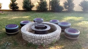 Un área de estar al aire libre circular con un brasero central, rodeada por ocho bancos hechos con neumáticos.