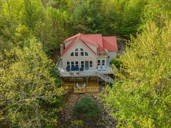 A large house with a red roof, multiple decks, and a porch with outdoor seating.