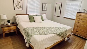 Une chambre à coucher bien rangée, avec un lit en bois, une table de chevet avec une lampe, une commode et des œuvres d’art encadrées accrochées aux murs.