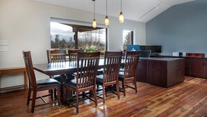 A dining area with a wooden table and chairs, a kitchen area with a counter and cabinets, and large windows offering a view of trees and mountains.