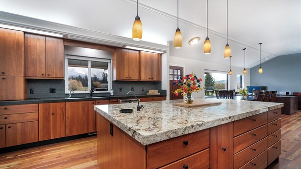 A spacious kitchen with wooden cabinets, a granite countertop, and pendant lighting.