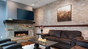 A modern living room with a stone fireplace, leather sofas, and a flat-screen TV mounted on the wall.