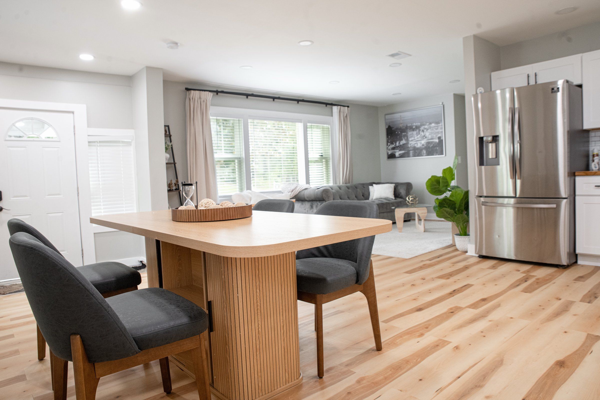 Una cocina moderna con refrigerador incorporado, un comedor con mesa de madera y dos sillas, y una sala de estar con sofá y mesa de centro.