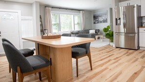 Una cocina moderna con refrigerador incorporado, un comedor con mesa de madera y dos sillas, y una sala de estar con sofá y mesa de centro.