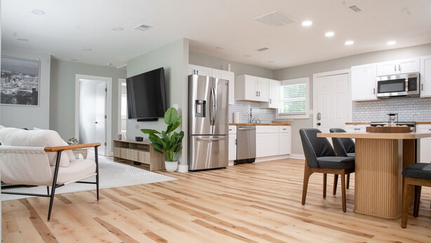 Una cocina moderna con armarios blancos, un refrigerador de acero inoxidable, un microondas y una mesa de comedor de madera con sillas.