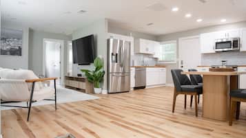 Una cocina moderna con armarios blancos, un refrigerador de acero inoxidable, un microondas y una mesa de comedor de madera con sillas.