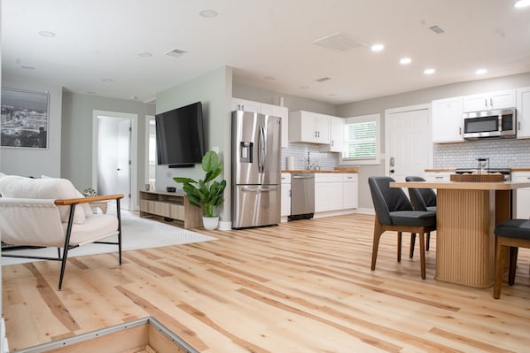 A modern kitchen with white cabinets, stainless steel appliances, and a wooden dining table.
