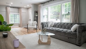 Una sala de estar moderna con un sofá gris, una mesa de centro de vidrio y una mesita auxiliar de madera.