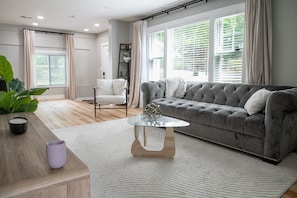 A modern living room with a grey sofa, a glass coffee table, and a wooden side table.