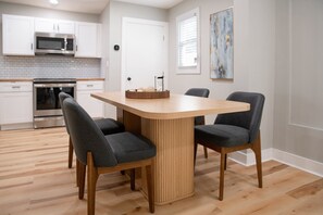 Une cuisine moderne avec des meubles blancs, des appareils en acier inoxydable et une table à manger en bois, accompagnée de quatre chaises.
