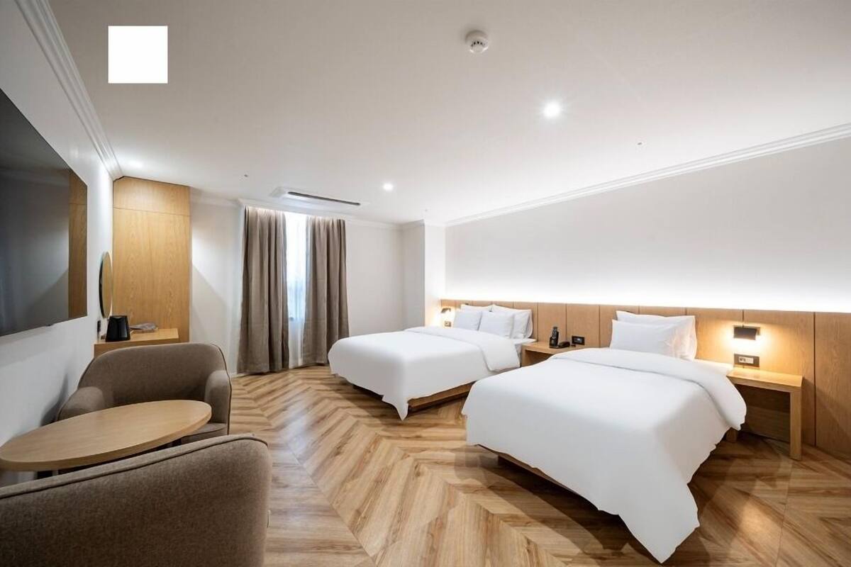 A hotel room with two beds, a sofa, a small table, and a large window with curtains.