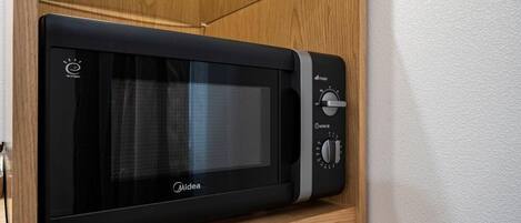 Un four à micro-ondes Midea noir, doté d’un écran numérique et de boutons de contrôle de la puissance, est posé sur une étagère en bois dans une cuisine.