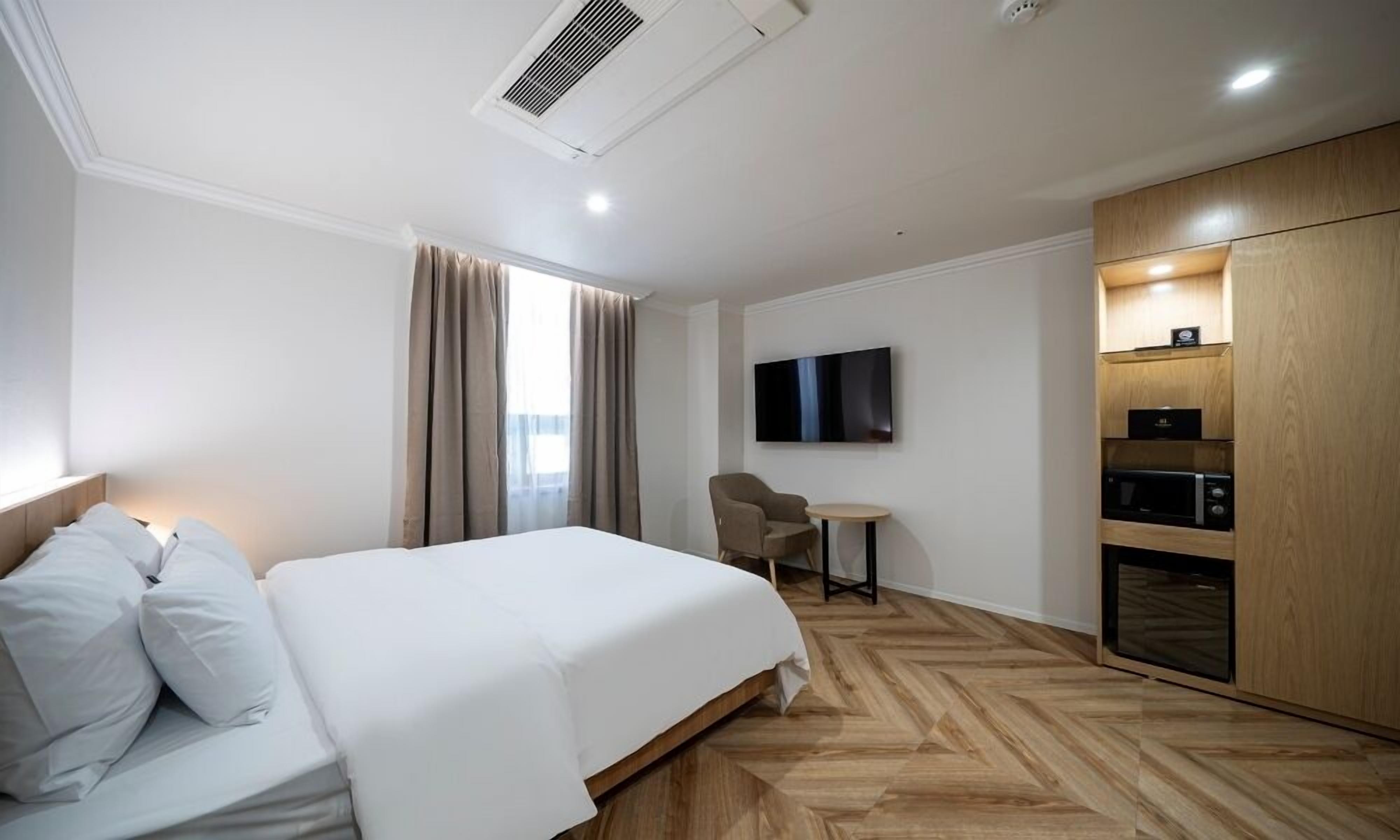 A hotel room with a bed, a desk, a TV, and a kitchenette.