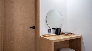 Una puerta de madera, un espejo redondo, una pequeña mesa de madera y un taburete.