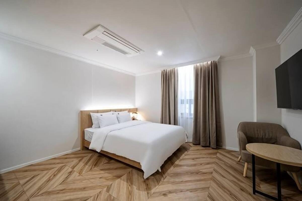 A hotel room with a bed, a chair, a TV, and a window with curtains.