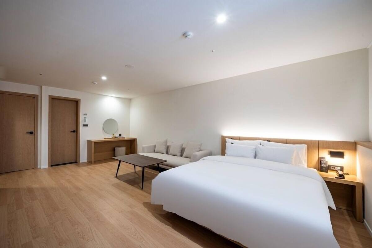 A hotel room with a bed, a sofa, a desk, and a mirror.