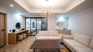 Una sala moderna con una mesa de centro de madera, sofás color crema y una lámpara de araña, con un portón corredizo de vidrio que da a un dormitorio.