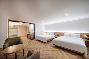 A hotel room with two beds, a sitting area with a table and chairs, and a sliding door leading to a balcony.