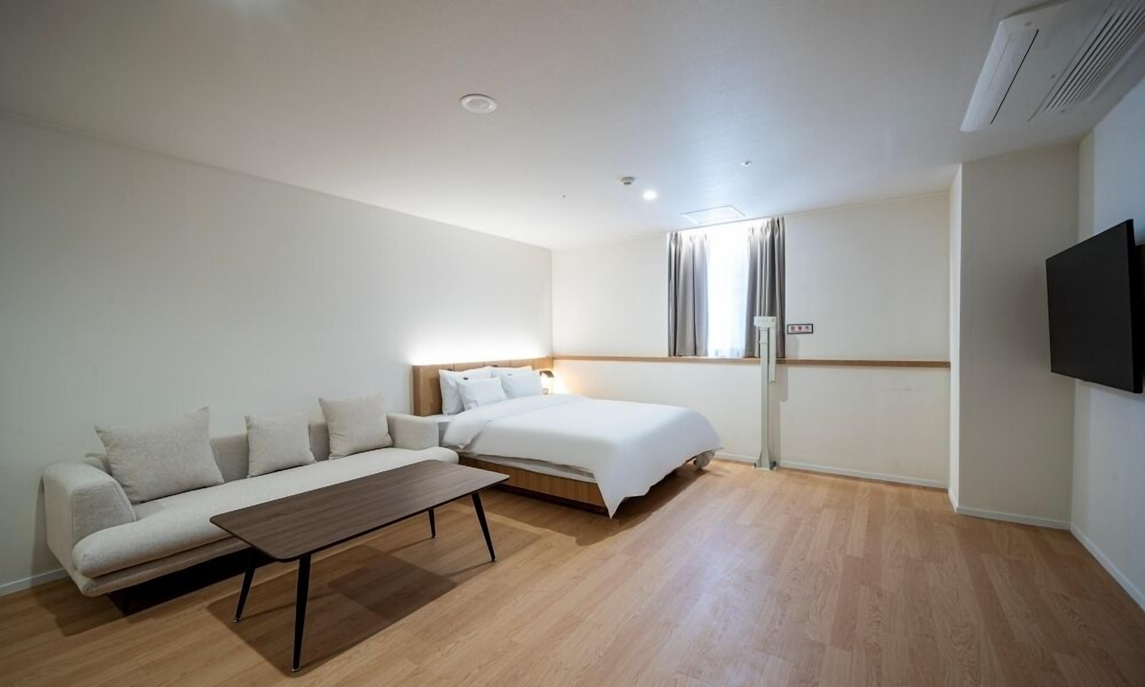 Ett hotellrum med en säng, en soffa, ett litet bord, en tv och ett fönster med gardiner.