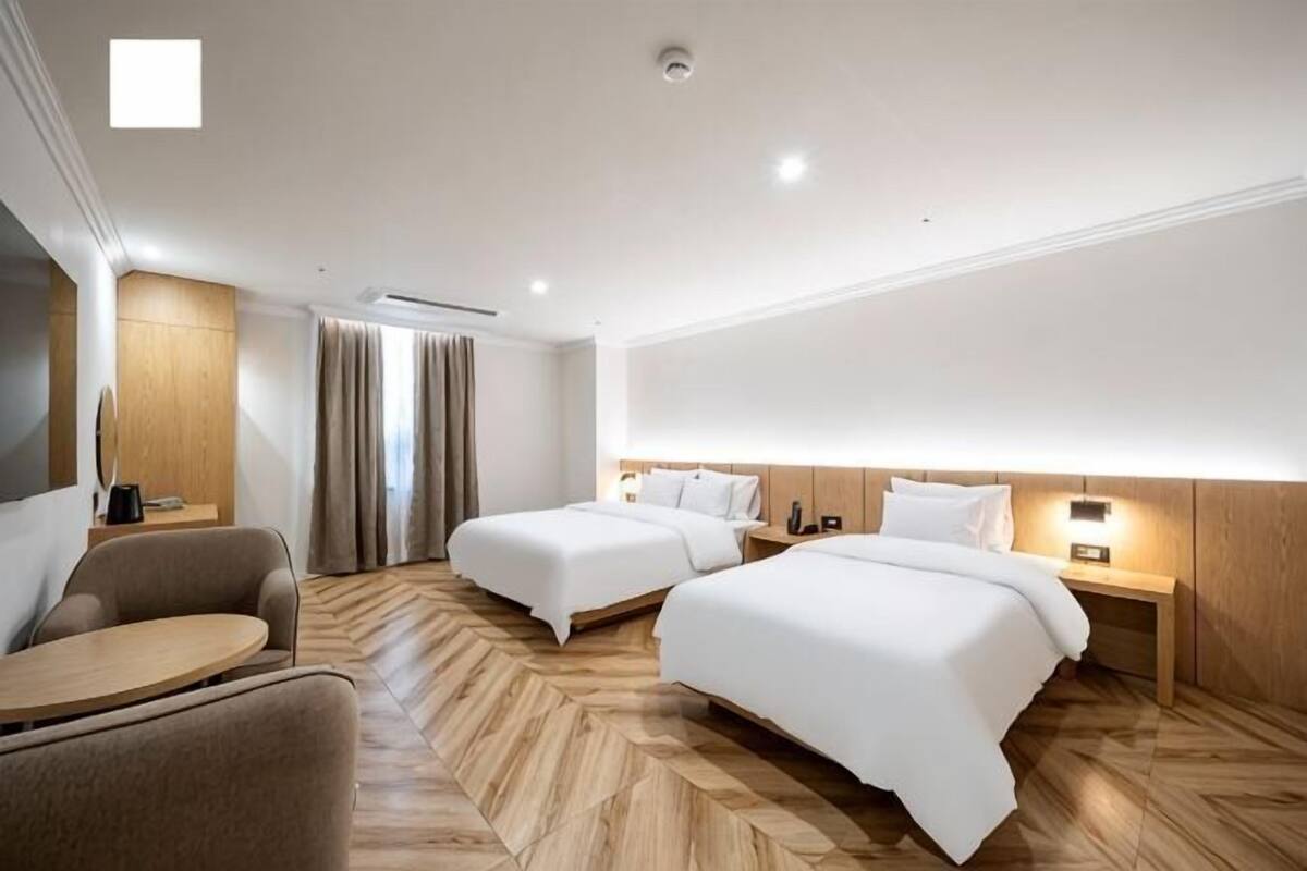 A hotel room with two beds, a sofa, a desk, and a TV.