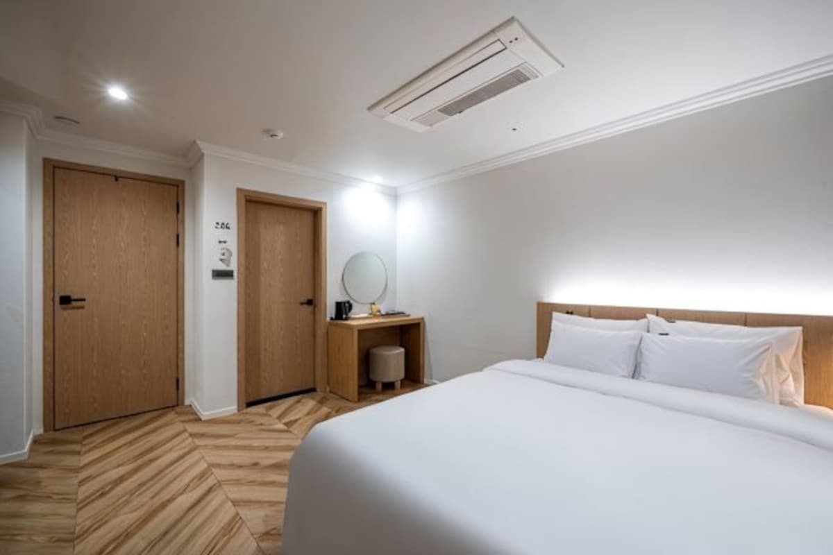 Habitación de hotel con cama, suelo de madera, escritorio con espejo y aire acondicionado de pared.