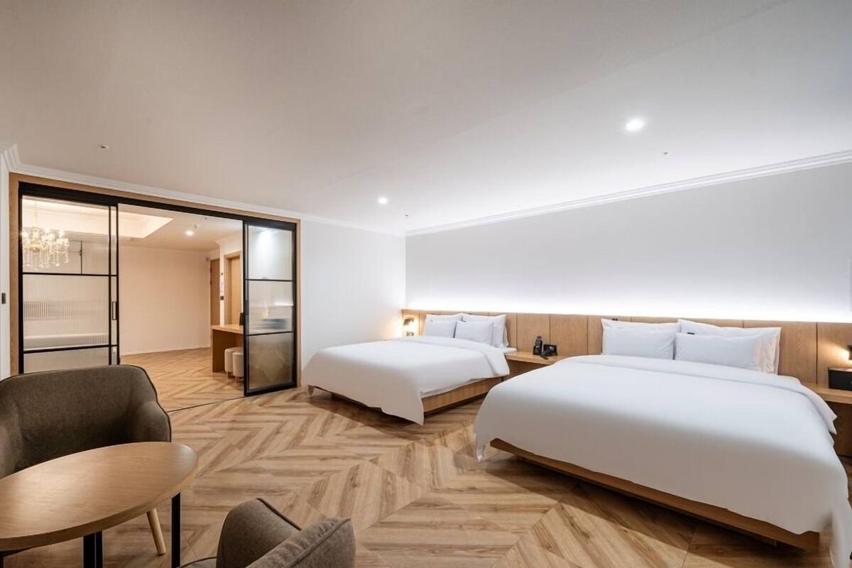 A hotel room with two beds, a seating area, and a sliding door leading to a bathroom.