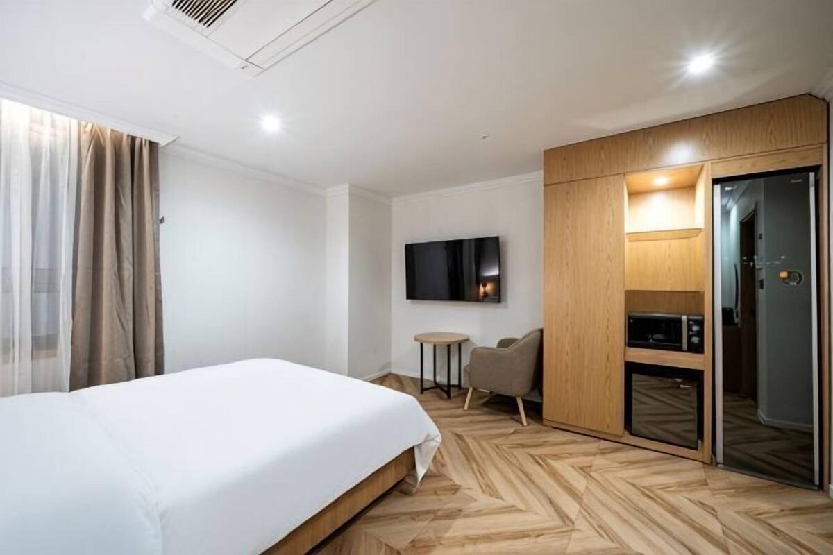 A hotel room with a bed, a television, a desk, a chair, and a wardrobe.