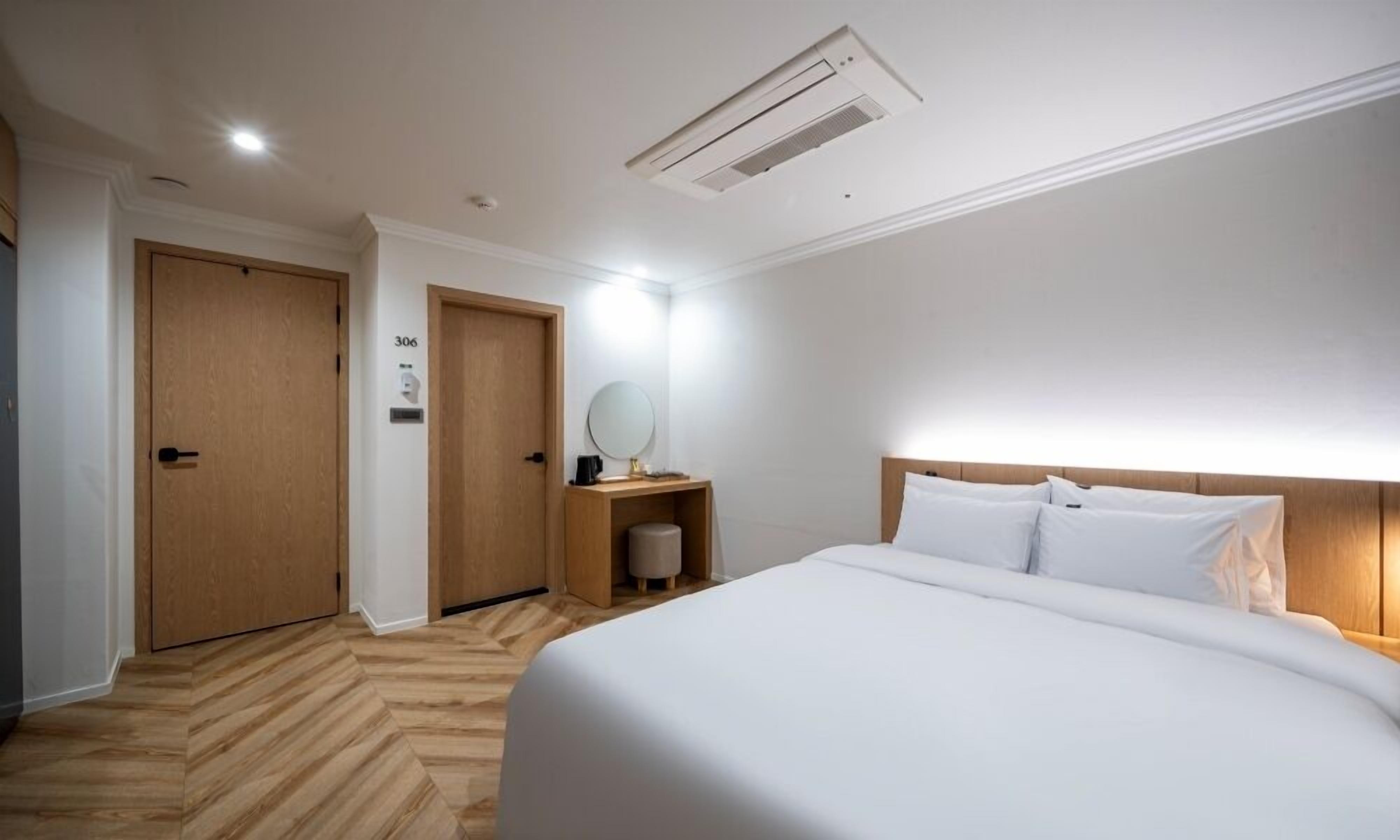 A hotel room with a large bed, wooden flooring, a desk with a mirror, and two doors.