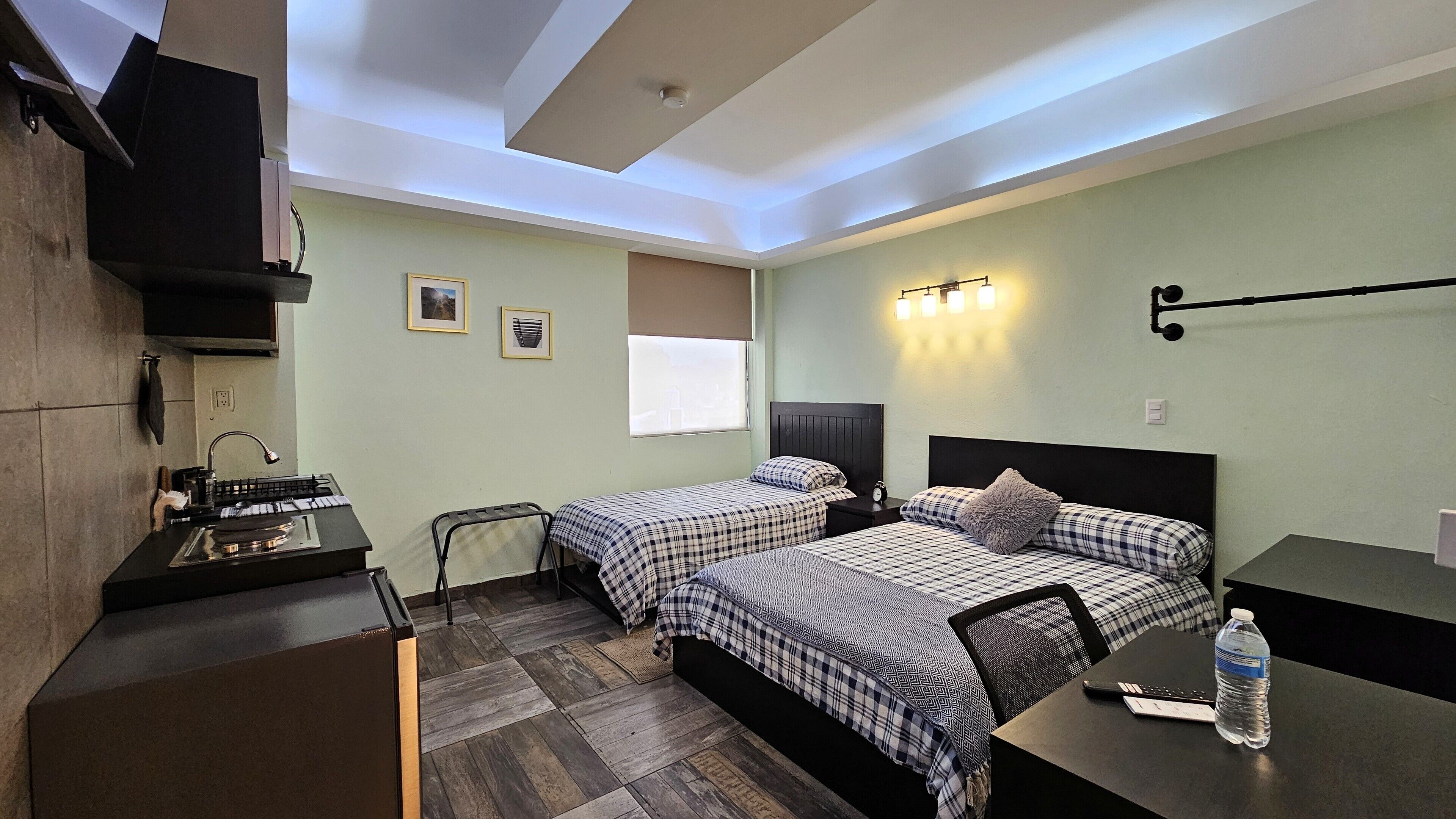 Habitación de hotel compacta con dos camas, un escritorio, una silla, una mesita y una botella de agua.