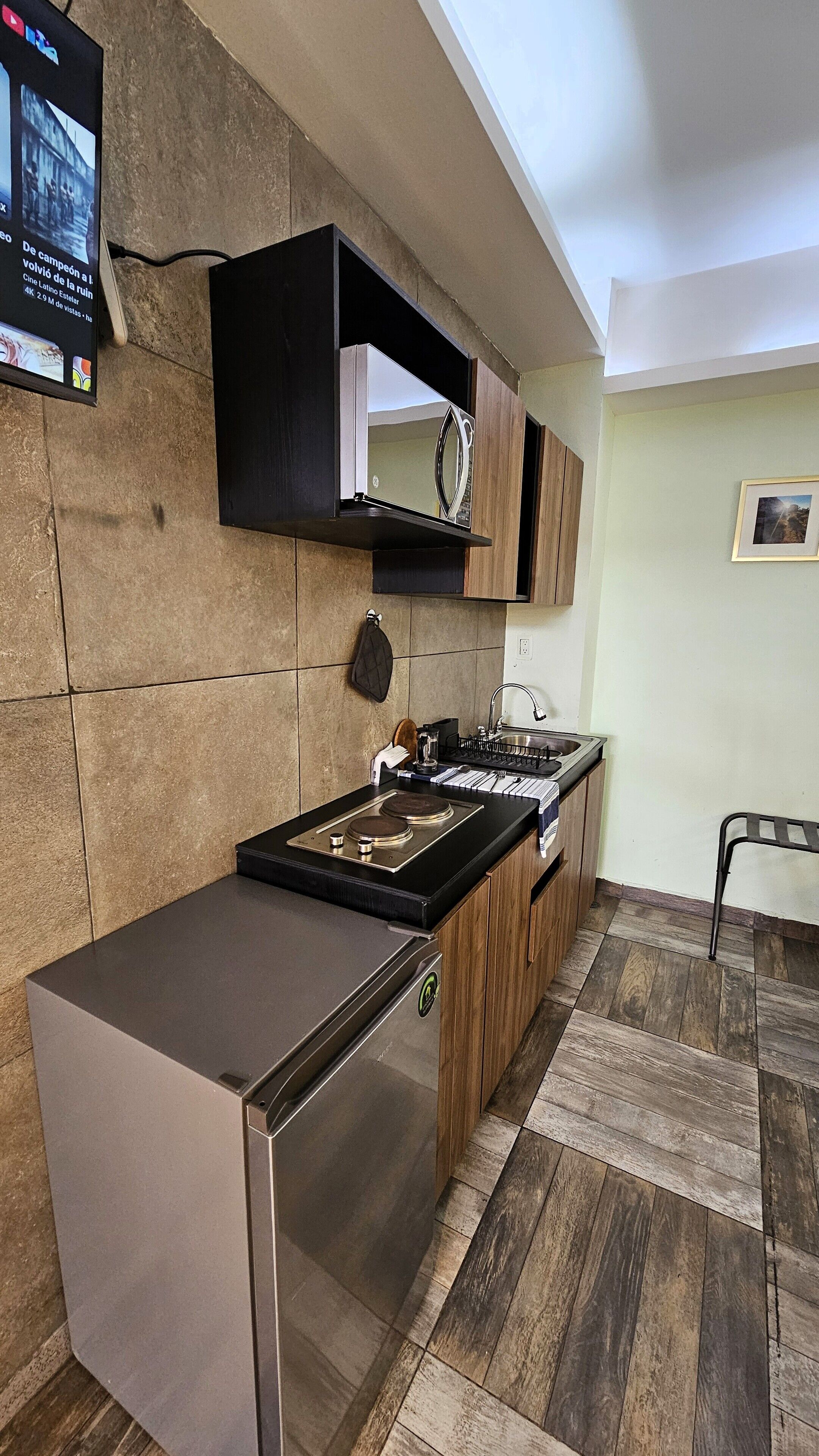 A modern kitchen with a built-in refrigerator, a stove, and a sink. There is a wooden cabinet above the stove and a small shelf. The kitchen has a tiled backsplash and a wooden floor.