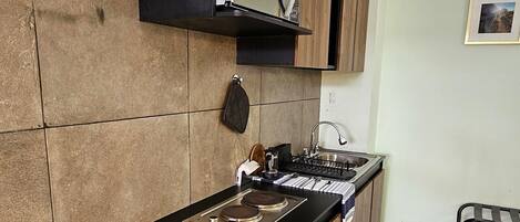 A modern kitchen with a built-in refrigerator, a stove, and a sink. There is a wooden cabinet above the stove and a small shelf. The kitchen has a tiled backsplash and a wooden floor.