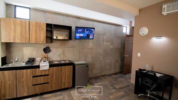 A modern kitchen with wooden cabinets, a built-in microwave, and a flat-screen TV displaying a game.