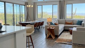 A spacious living area with a large window overlooking a desert landscape, a dining area with a view, and a kitchen with a central island.