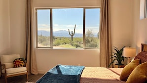 A bedroom with a large window, a bed, a chair, and a lamp.