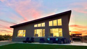 A modern two-story building with large windows, a flat roof, and a patio area with outdoor seating.