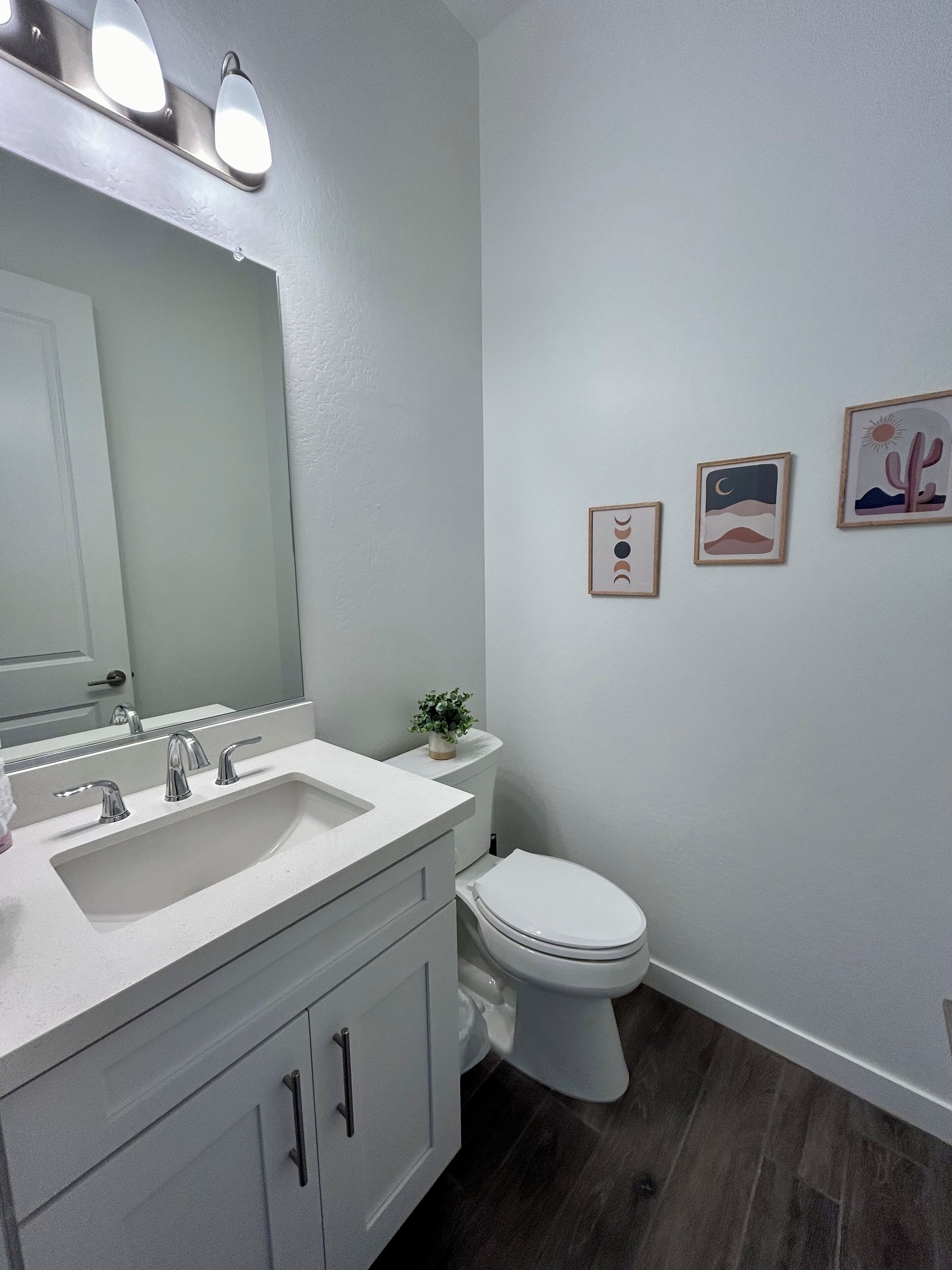 A bathroom with a white sink, mirror, and toilet. There are three framed pictures on the wall.