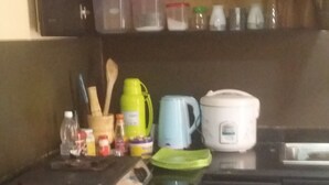 Cocina compacta con cubierta negra, microondas, hervidor y diferentes utensilios y recipientes de cocina.